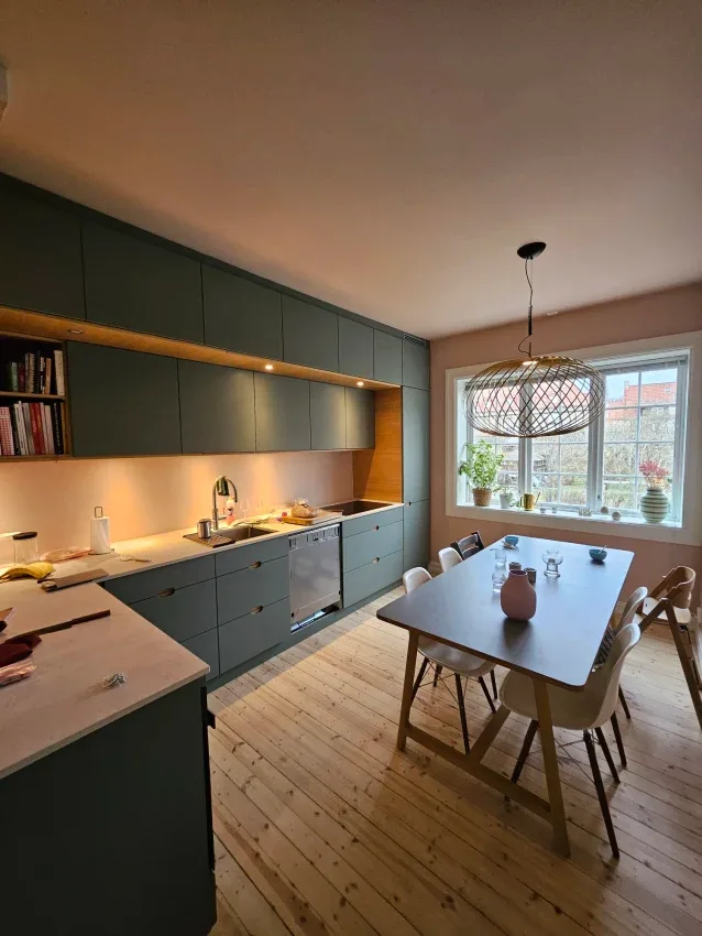 Kjøkken med grønne fronter og spisebord ved vinduet